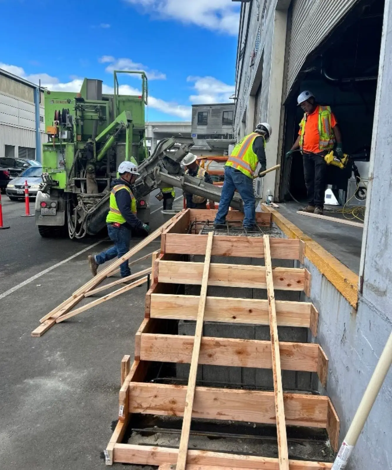 Crew in hi-viz placing concrete with pump truck and wood formwork